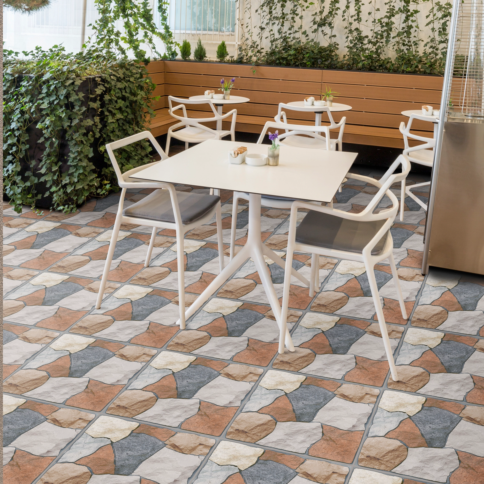 Exterior terraza, mesas blancas, reposador de madera, adornado con plantas en el borde y piso de cerámica piedra Valterra, colección Ecos de Cerámicos Gala
